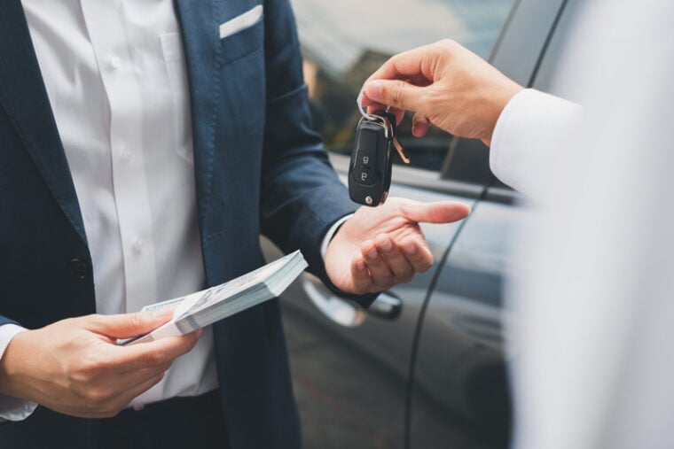 Ein*e Autoverkäufer*in überreicht den Schlüssel eines Autos an eine*n Kund*in.