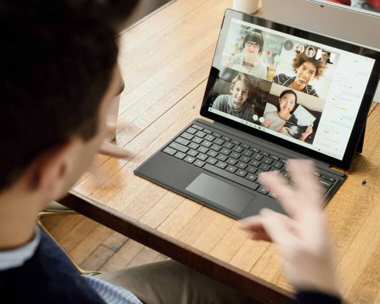 Mann sitzt am Tisch und ist mit seinem Laptop in einem meeting in dem er mit seinen Kollegen spricht