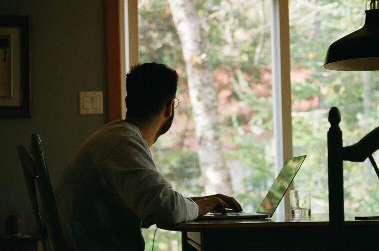 Ein Mann sitzt am Schreibtisch vor seinem Laptop und schaut aus dem Fenster