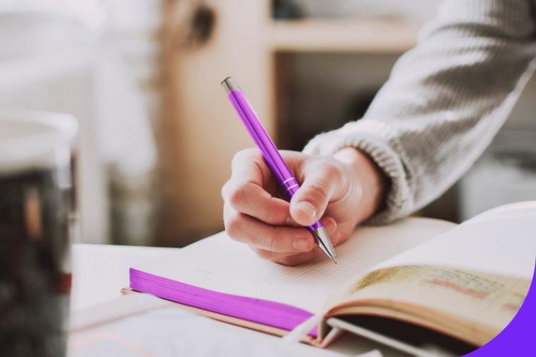 Eine Nahaufnahme zeigt die Hand einer Person, die mit einem pinken Stift ein Tagebuch ausfüllt.