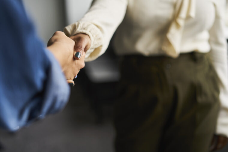 Eine Nahaufnahme zeigt einen Handschlag zwischen zwei Personen auf der Arbeit.