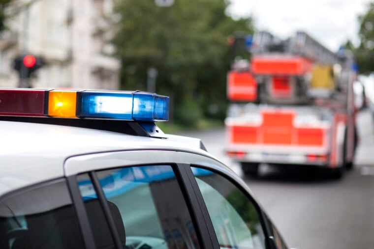 Das Bild zeigt das Blaulicht eines Polizeiautos mit einem Feuerwehrwagen im Hintergrund.