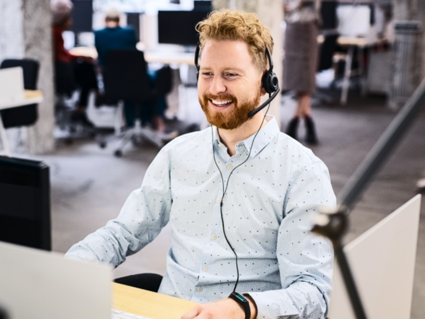 Ein Kundendienstmitarbeiter sitzt in einem Büro und spricht per Headset am Telefon.