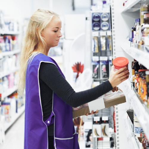 Eine junge Frau räumt im Rahmen einer kurzfristigen Beschäftigung im Supermarkt Regale ein.