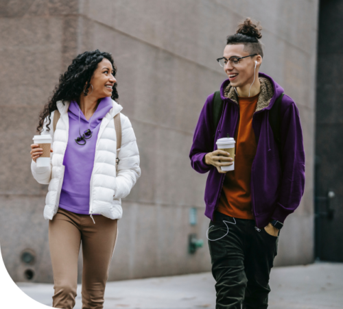 Eine junge Frau und ein junger Mann laufen durch die Stadt. In ihrer Hand befindet sich ein Coffee-to-go.