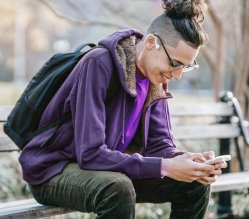 Ein junger Mann nutzt sein Smartphone auf einer Bank im Park.