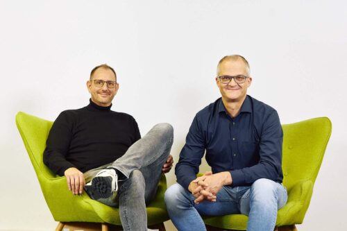 Oliver Klein, Teamleitung Inbound bei KiM, und Bernhard Fritzenschaft, Teamleitung Inbound Prokurist bei KiM, sitzen auf einer grünen Couch