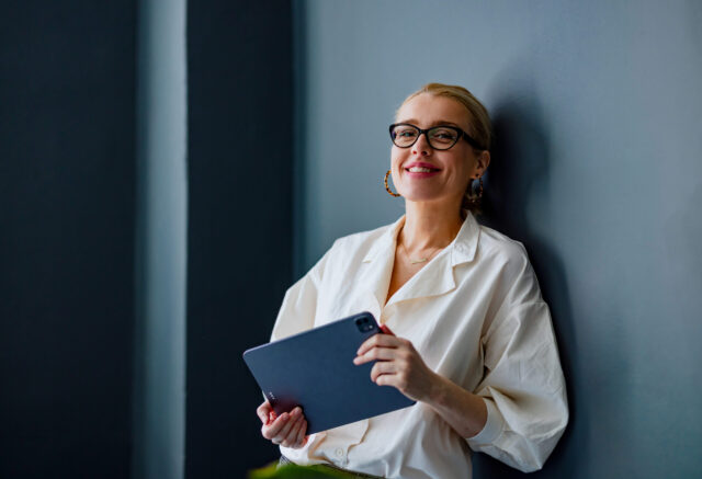 Frau mit Tablet in der Hand lehnt an einer Wand