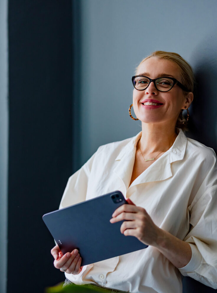 Frau mit Tablet in der Hand lehnt an einer Wand