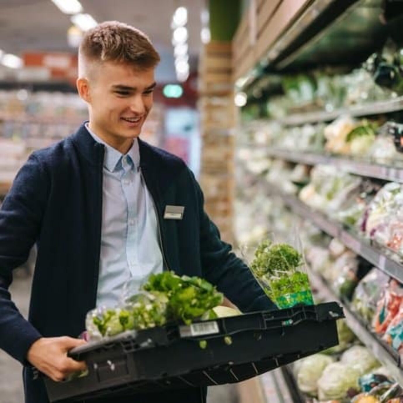 Student working in a supermarket, restocking the shelves with salad