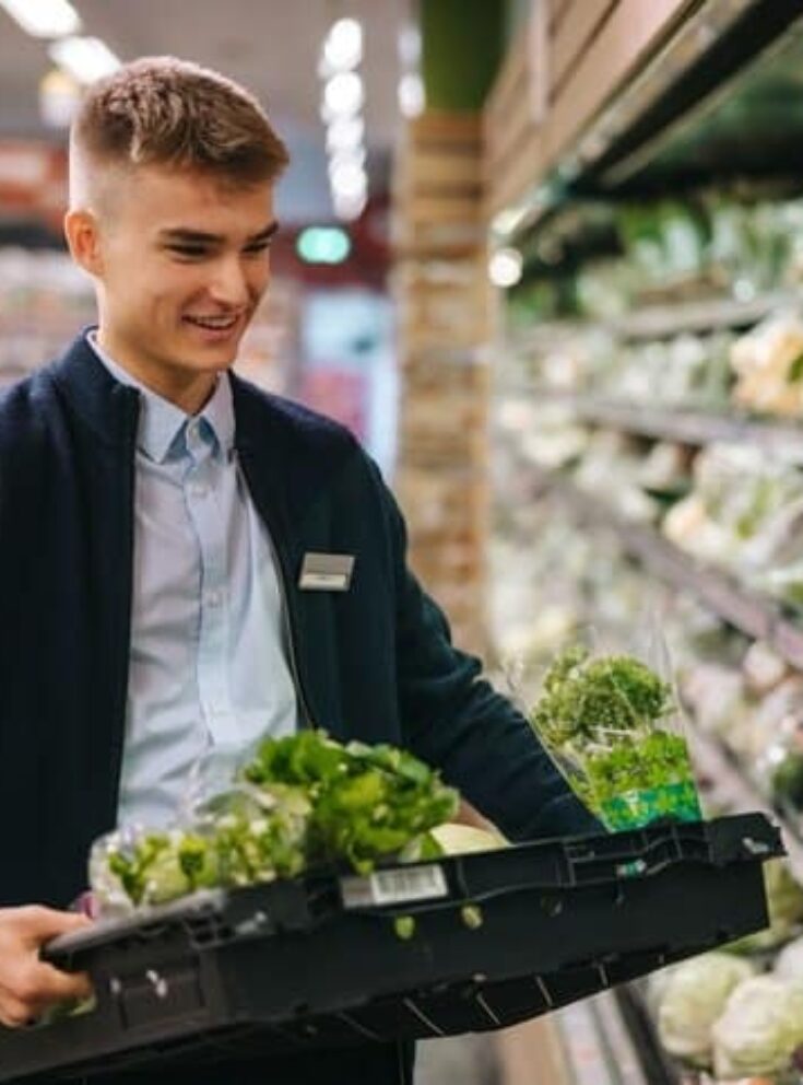 Student working in a supermarket, restocking the shelves with salad