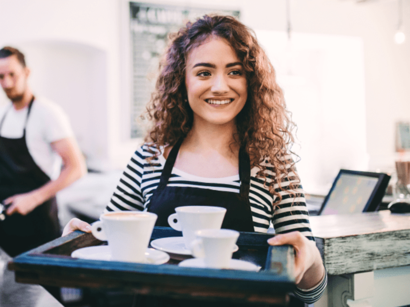 A young waitress is carrying three cups on a tray.