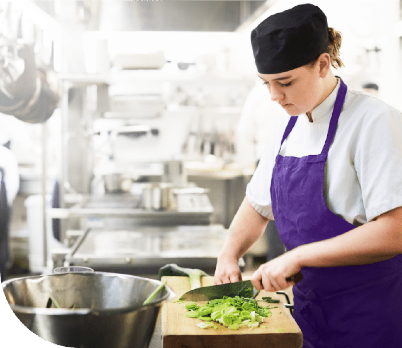 The image shows a young woman cut food in a kitchen.