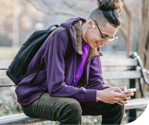 A young man is using his smartphone on a bench in a park.