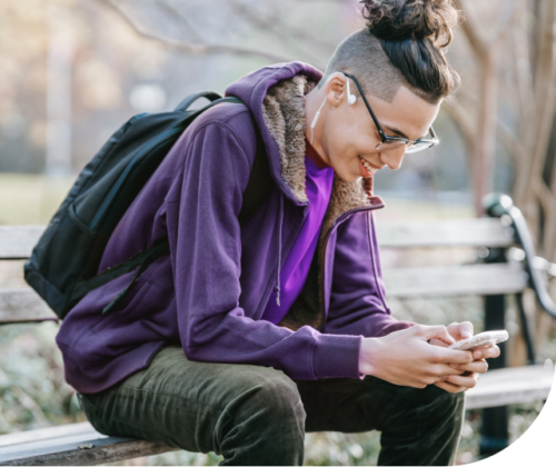 A young man is using his smartphone on a bench in a park.