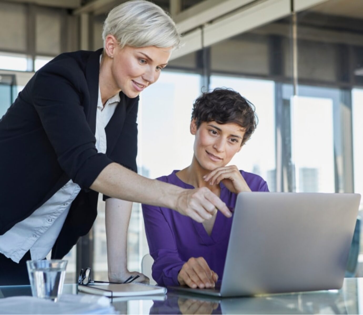 A woman shows another woman sitting at a laptop how Zenjob works.