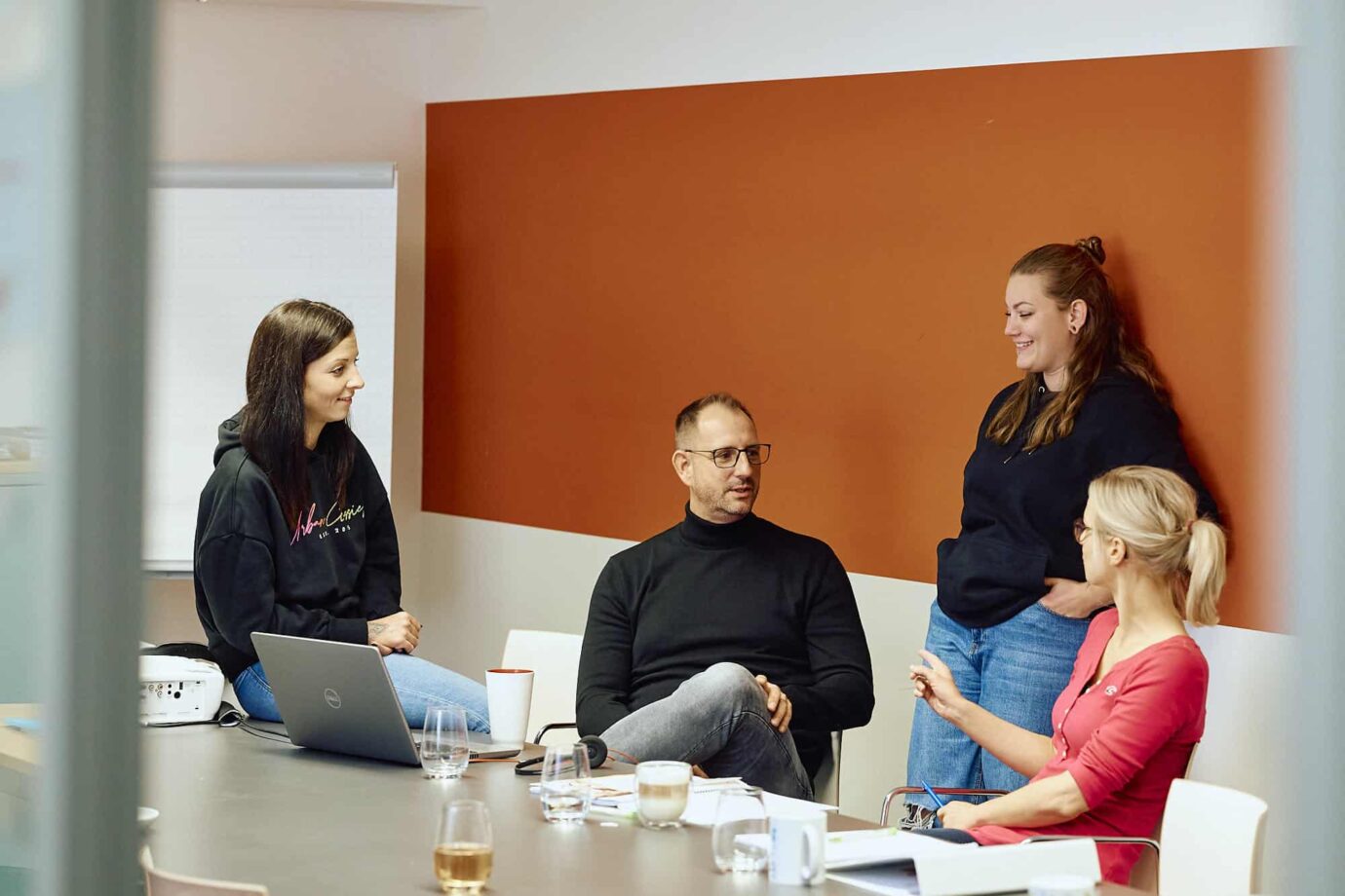 Four customer support team members of KiM sitting and standing in a meeting room